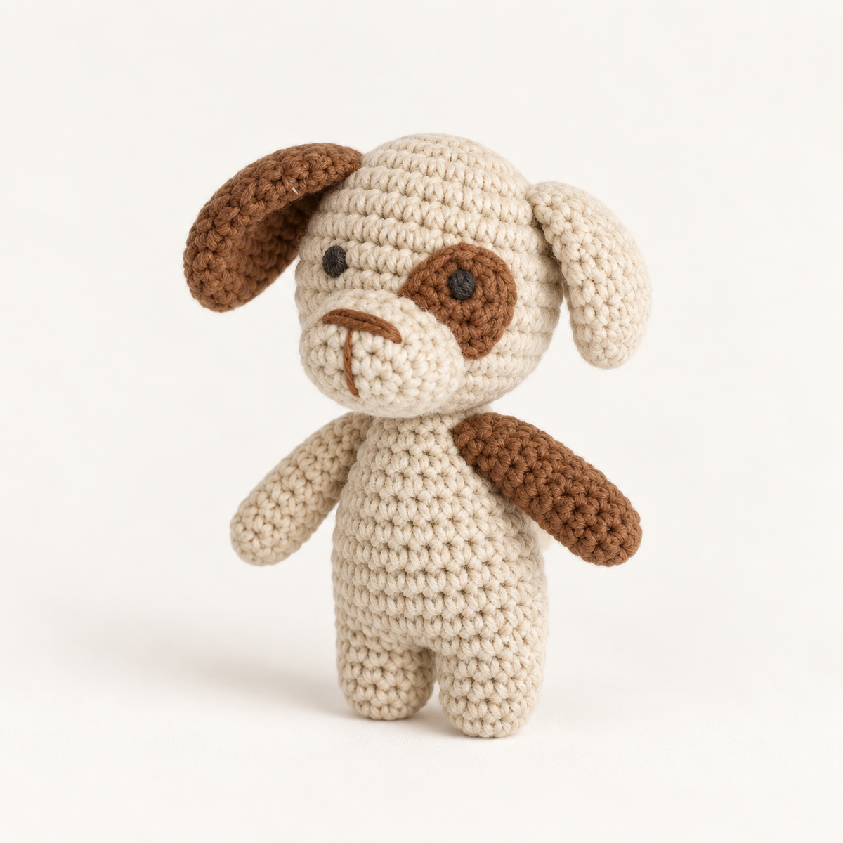 Cream hand-crocheted dog toy with brown ears, a brown eye patch and brown paw details