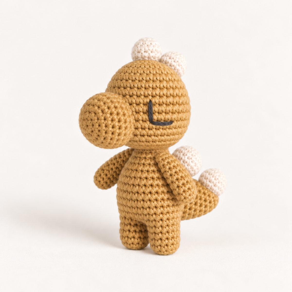 Mustard-yellow hand-crocheted dinosaur toy with cream-coloured spikes