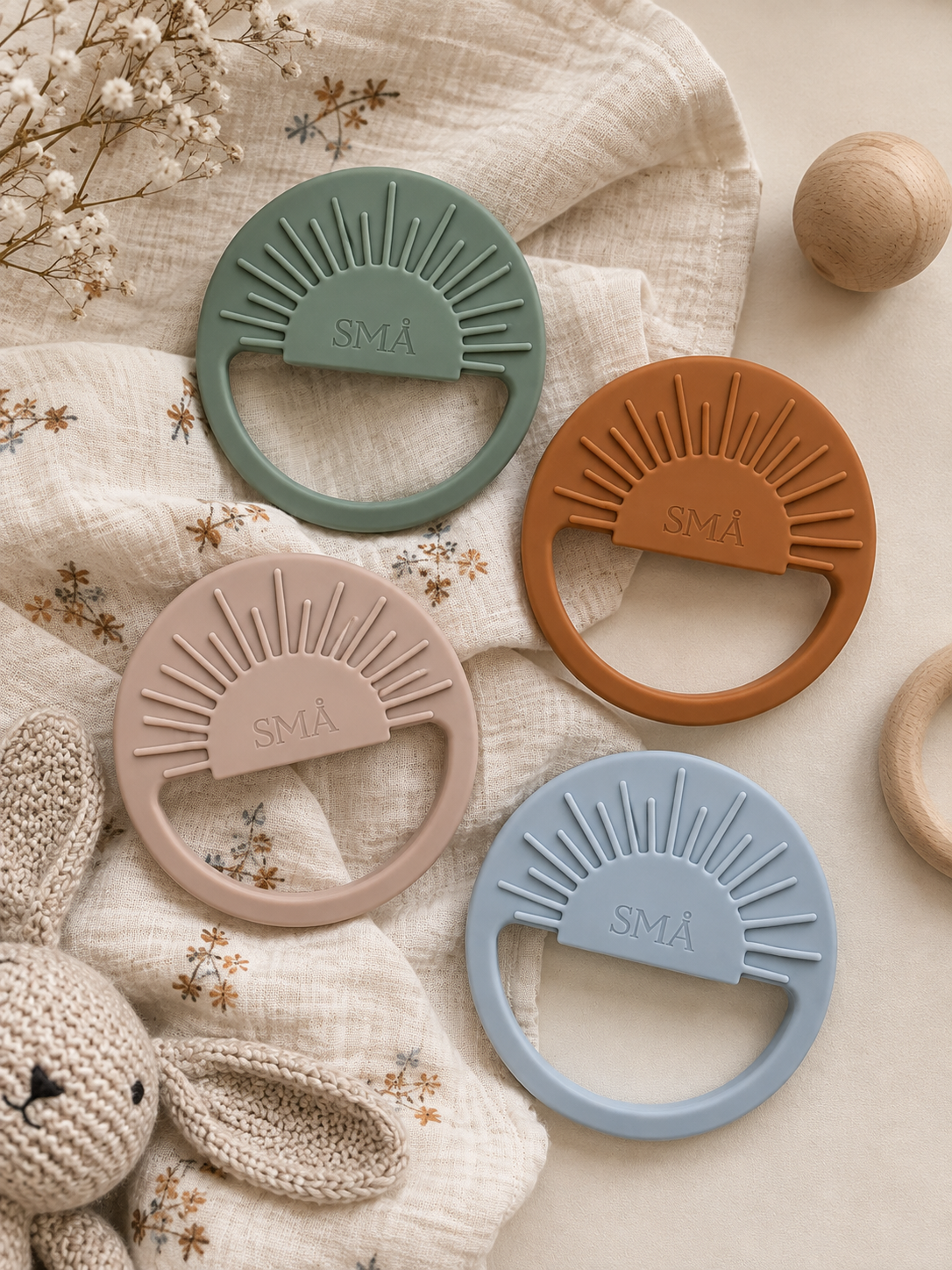 SMÅ Sun Baby Teethers in light gray, sand, caramel and eucalyptus arranged on a cream background