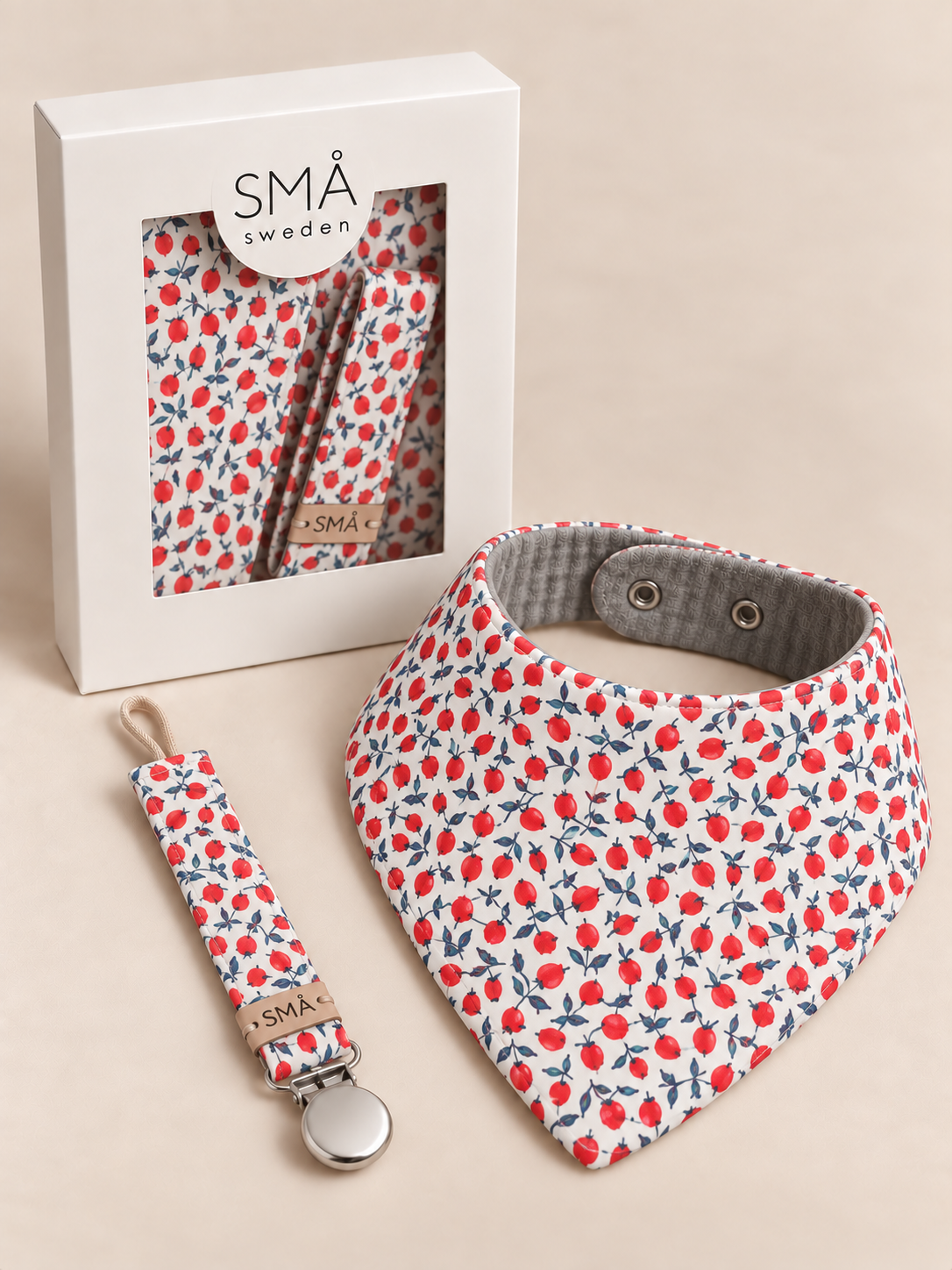 MÅ baby bib and matching pacifier clip in red berry and navy botanical print displayed with the gift box