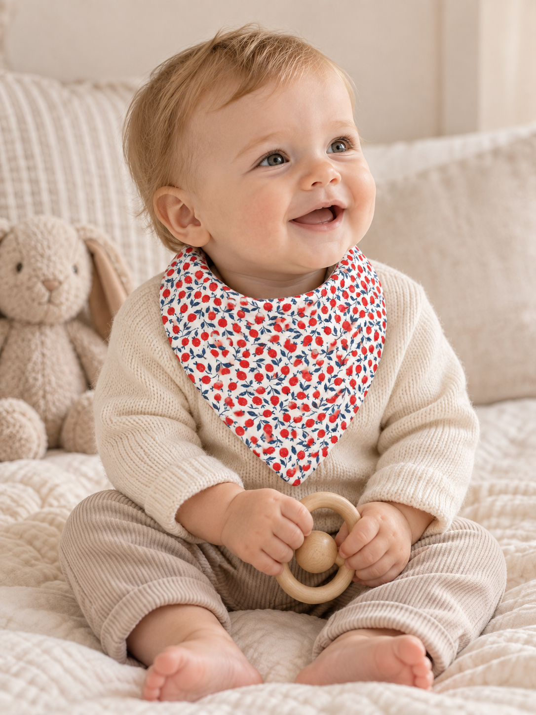 Baby boy wearing a SMÅ baby bib in Liberty-style red berry and navy botanical print, photographed in a warm neutral nursery
