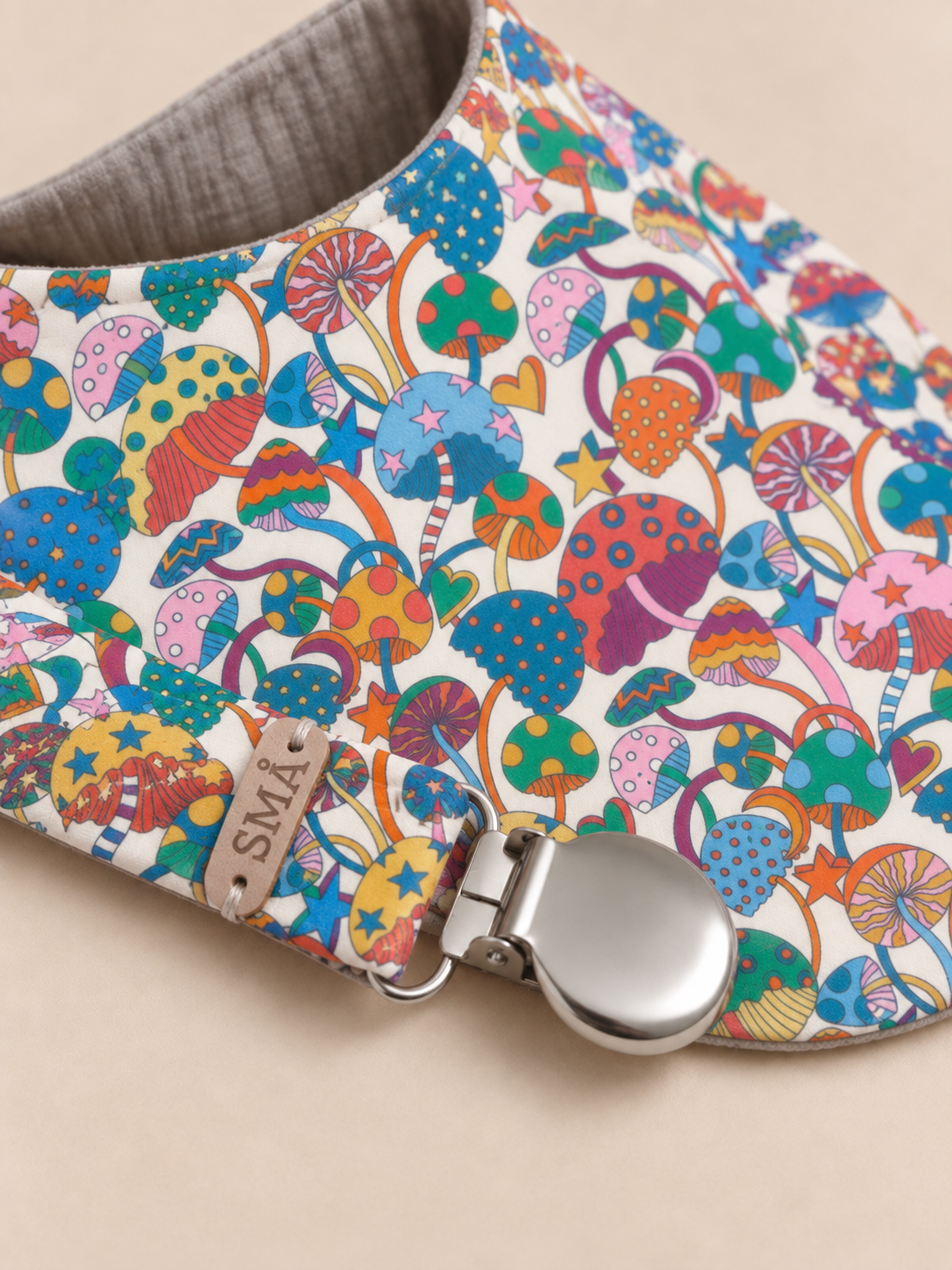 Close-up of Liberty Magic baby bib and matching pacifier clip showing fabric detail, leather SMÅ label and silver metal clasp