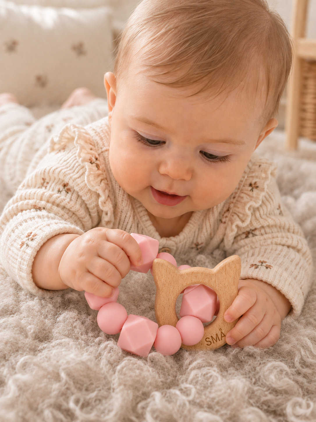 Baby holding and exploring the SMÅ Kitty Baby Teether in pink silicone and beech wood