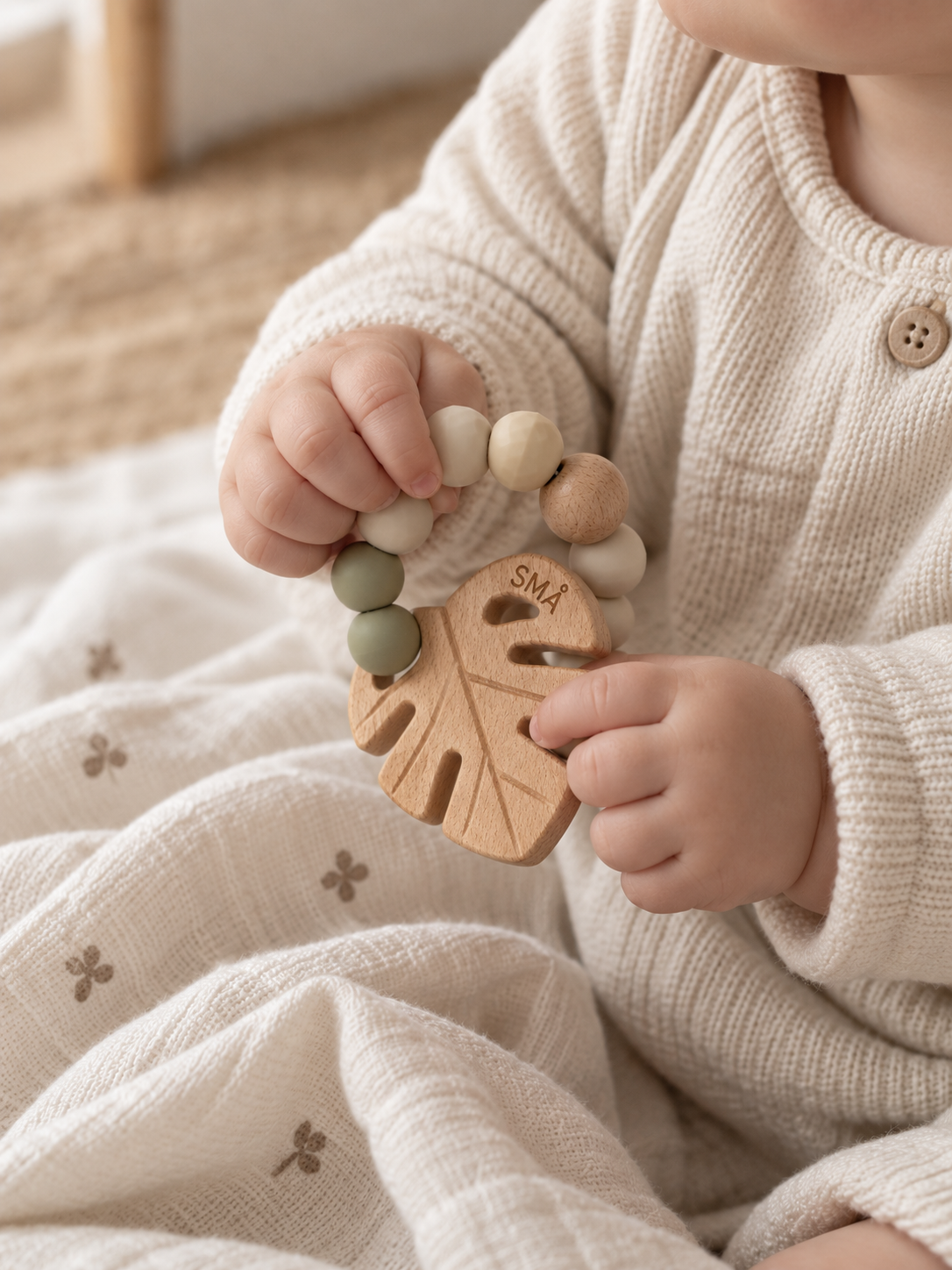 Baby holding the SMÅ Leaf Baby Teether with natural beech wood and sage green silicone beads