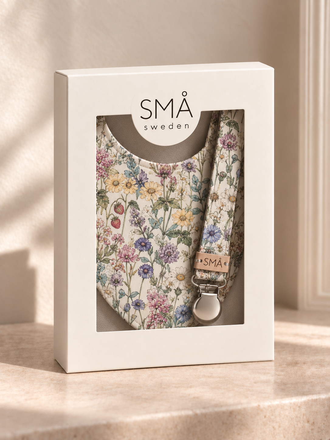 A floral-patterned baby bib and matching bandana set in a white window box packaging, with the brand name 'SMÅ sweden' visible on the box and bandana.